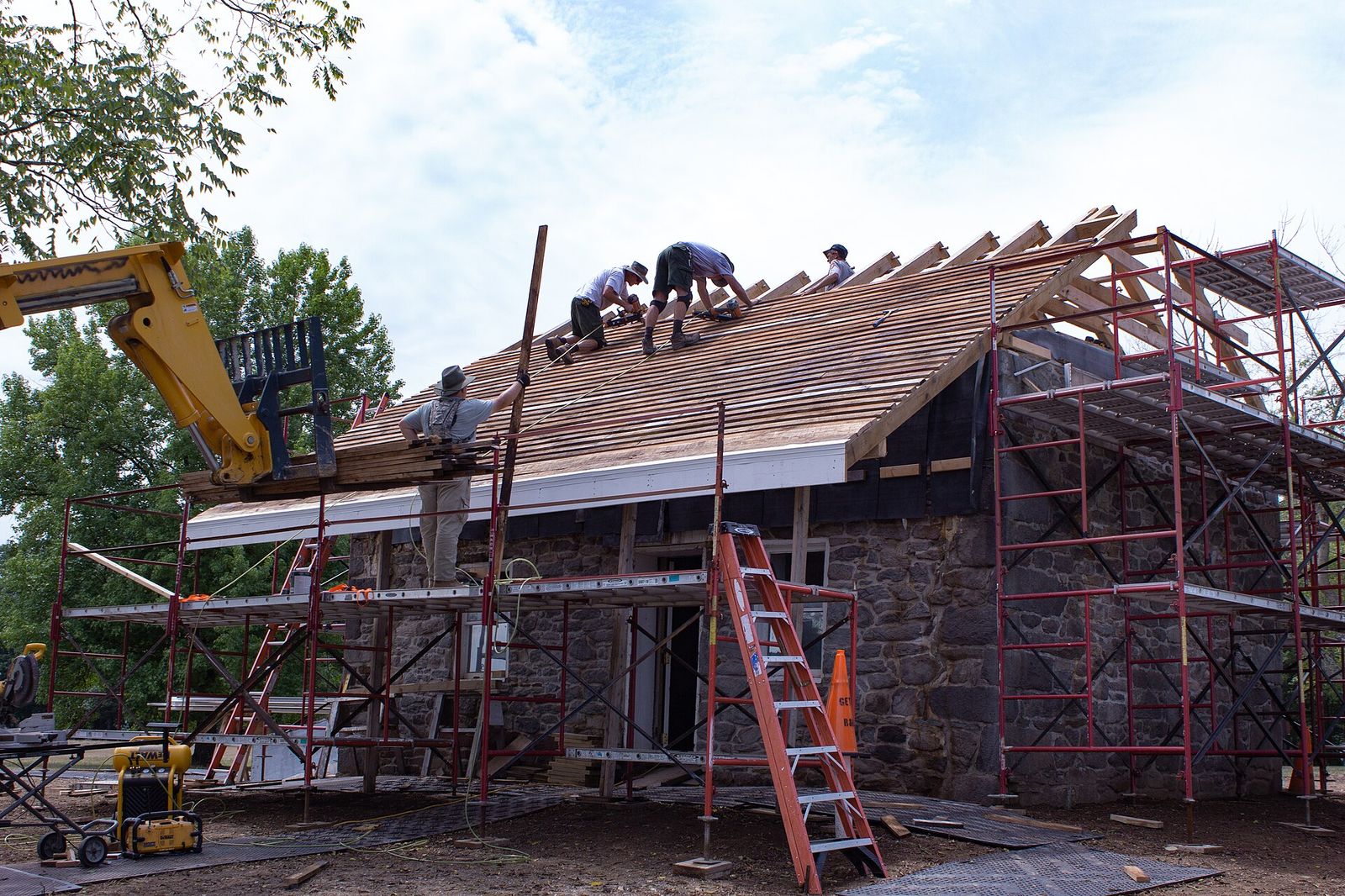 Roofing crew near the ridge of a steep roof, bundles going up on a telehandler