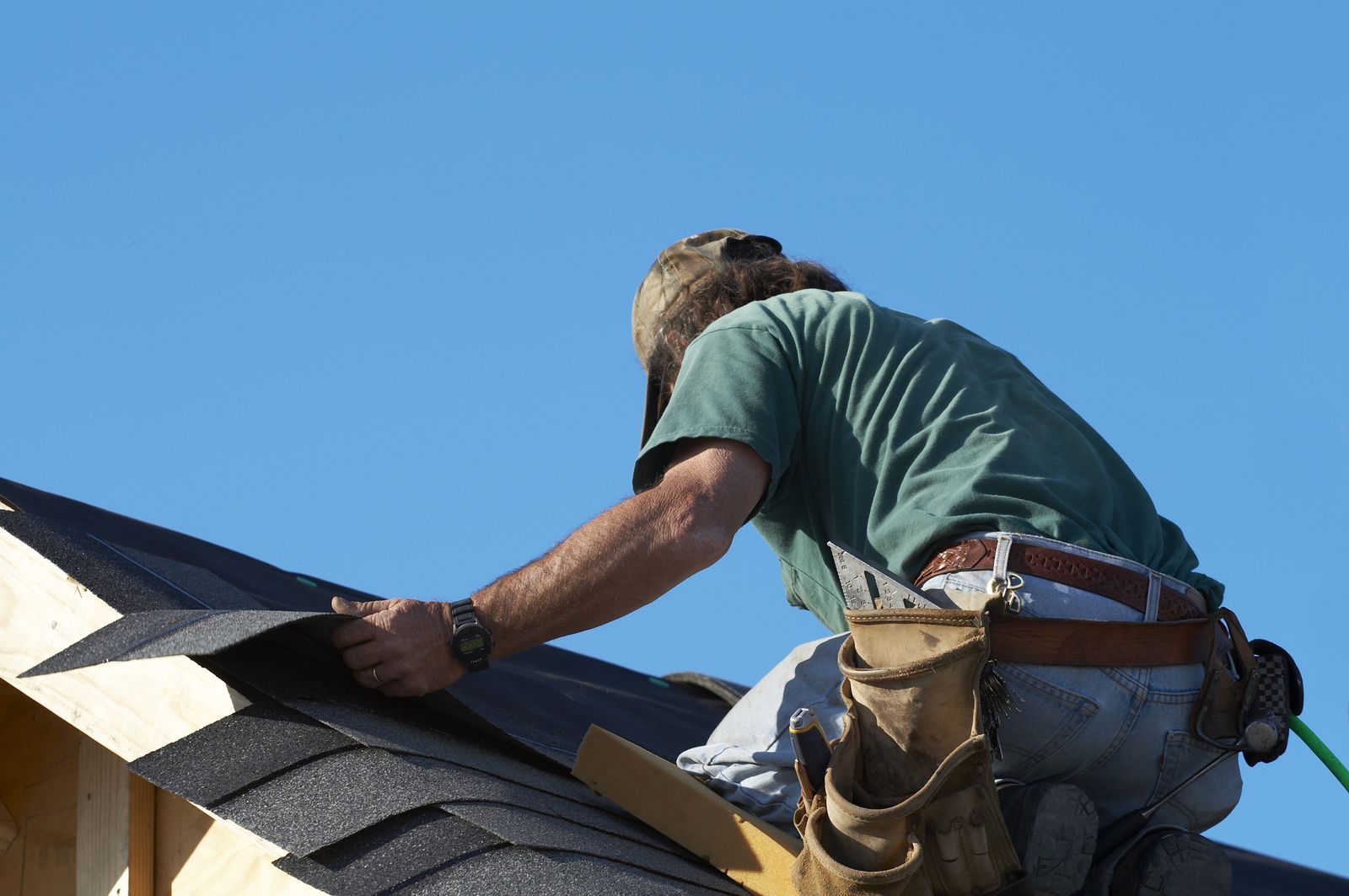 Roofer fastening architectural shingles along the eave of a pitched roof